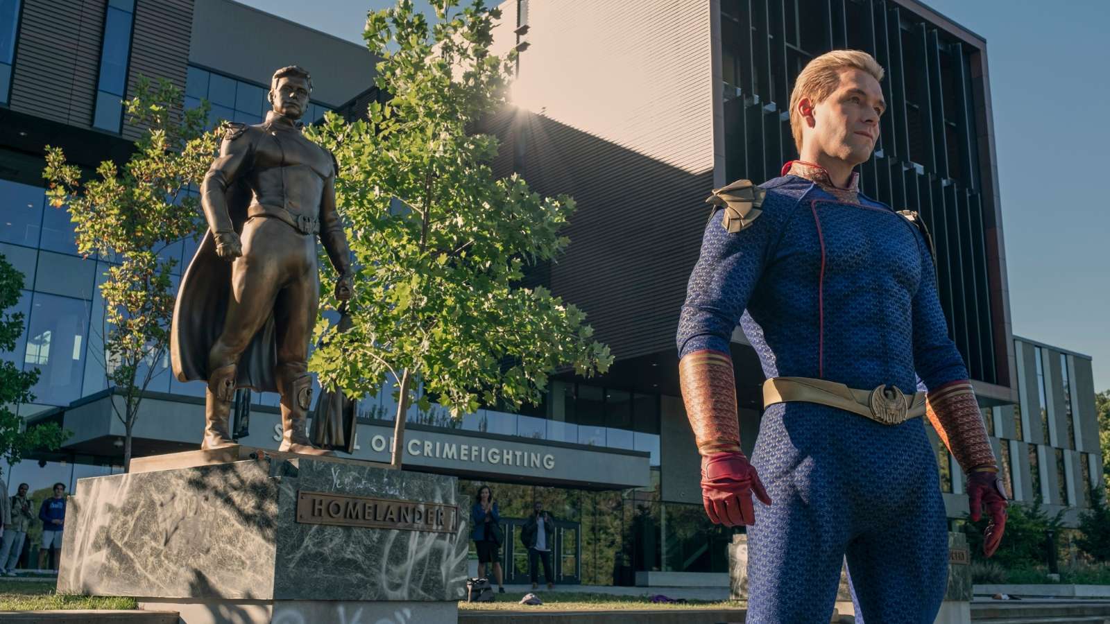 homelander se tient devant une statue de lui-même, devant une université