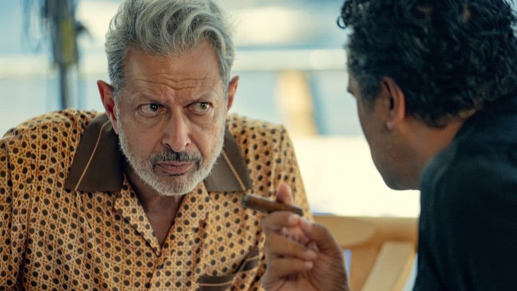 zeus alias jeff goldblum écoute avec attention poséidon tenant un cigare dans sa main